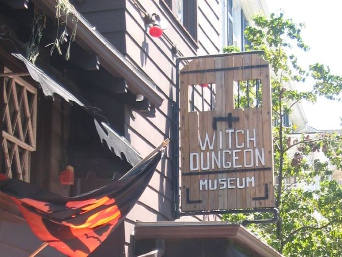 A sign for the witch dungeon museum hangs from the side of a building