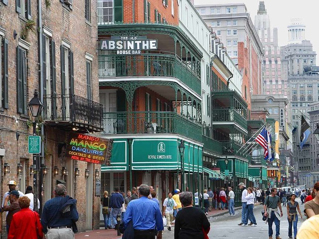 A crowd of people are walking down a street in new orleans in front of a building that says absinthe