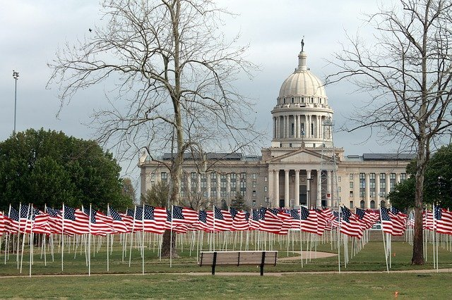 A row of american flags in front of a the oklahoma state capitol building in oklahoma city