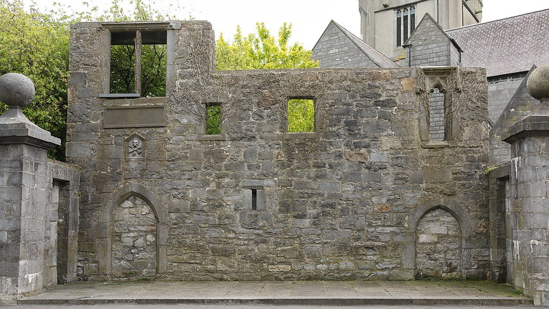 A stone wall with arches and the Lynch Memorial Window in front of a church.