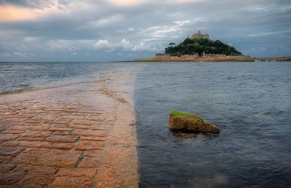 A stone walkway leading to the small island in the middle of the ocean that is home to St Michaels Mount