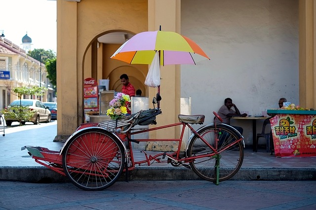 A rickshaw with a colorful umbrella is parked on the side of the road in penang