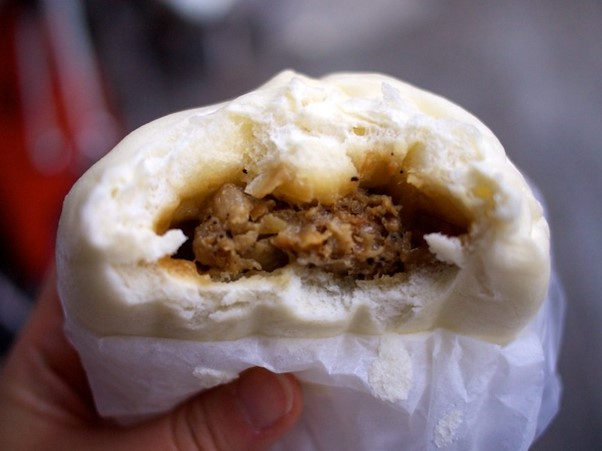 A person is holding a steamed bun with meat inside of it.