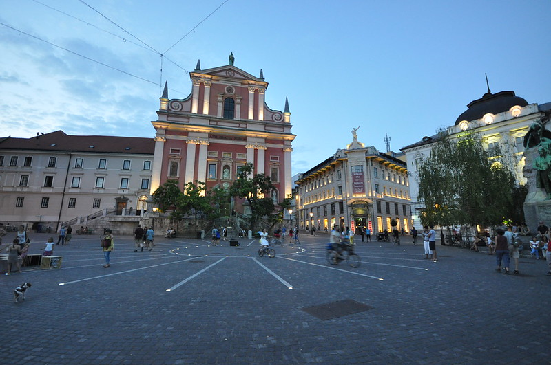 A group of people are walking in Prešeren Square in Ljubljana in front of a large building.