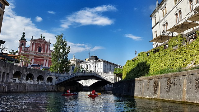 Two people are rowing kayaks down a river under a bridge in ljubljana