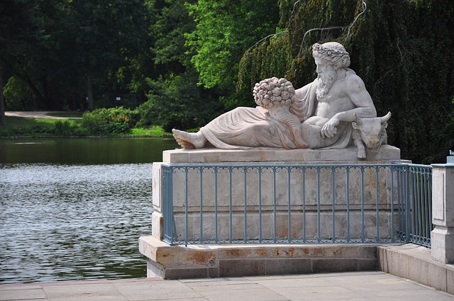 A statue of a man laying on a turtle next to a lake in Lazienki Park