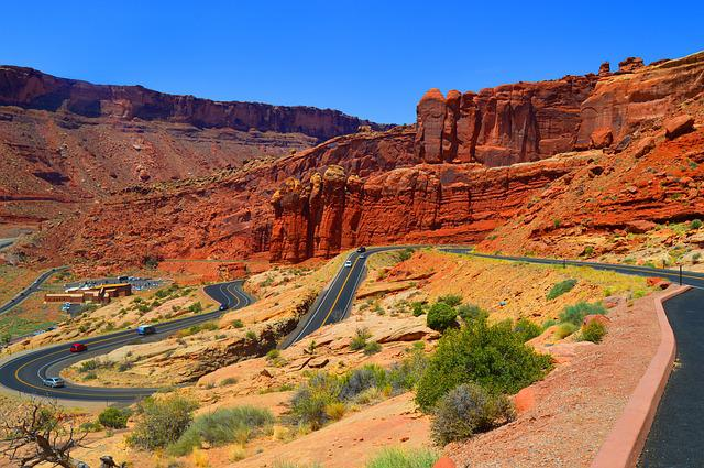 A winding road going through a desert landscape in Utah with mountains in the background.
