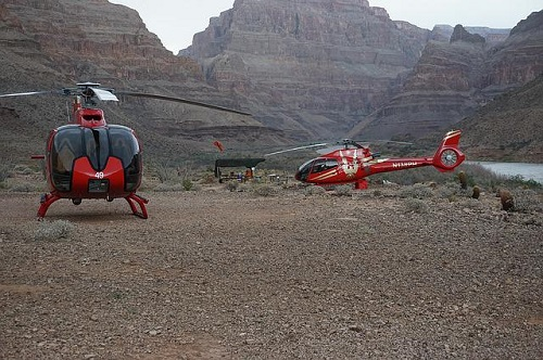 Two helicopters are parked in the desert near a river in the grand canyon