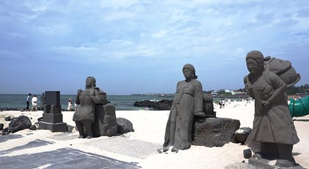 A group of statues are standing on a beach near the ocean in jeju