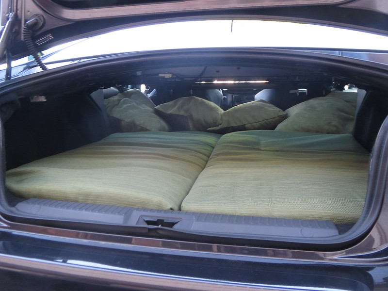 The trunk of a car with a bed and pillows in it