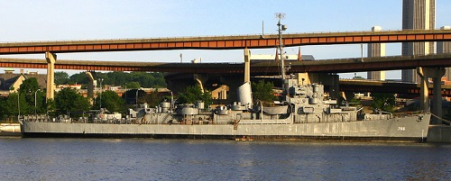 The USS slater is docked under a bridge in the water
