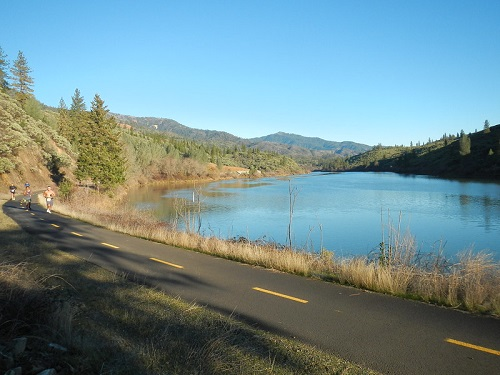 A person is riding a bike on a road next to a lake.