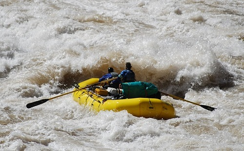 A yellow raft is going through a rapid river in the grand canyon