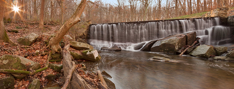 A waterfall in the middle of a forest with the sun shining through the trees in Susquehanna State Park