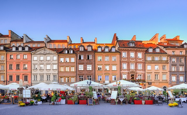 A row of buildings in warsaw with tables and umbrellas in front of them.