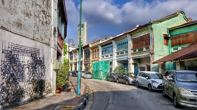 A narrow street in penang with cars parked on the side of it