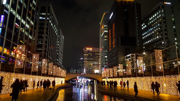 A group of people are walking along a river in Seoul at night.
