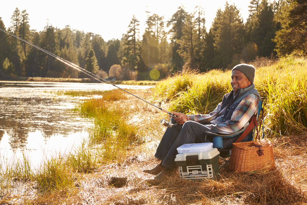 A man is sitting on a chair fishing in a lake in redwood np.