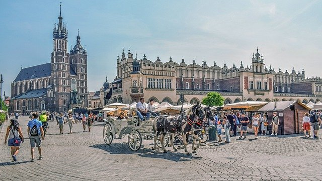 A horse drawn carriage is driving down a cobblestone street in front of a church in Krakow