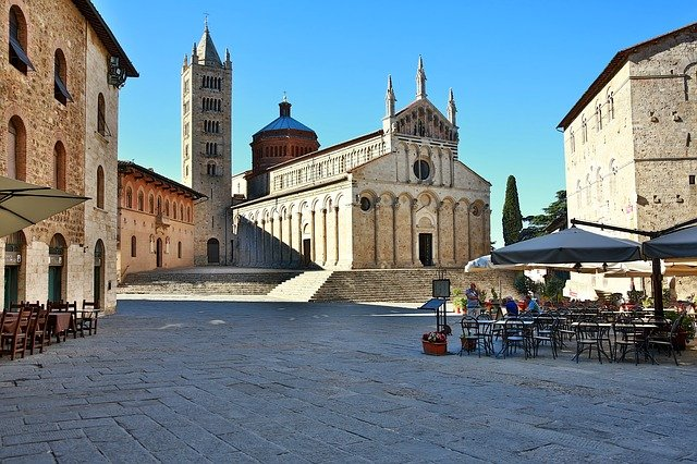 A city square in Tuscany with tables and chairs in front of a large church.