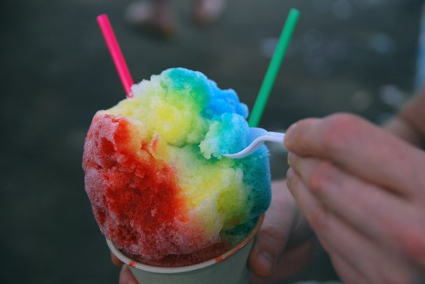 A person is eating a rainbow colored shaved ice with two straws