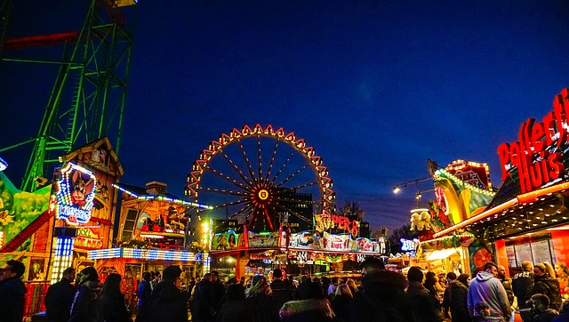A crowd of people are walking around winter dom at night with a ferris wheel in the background.