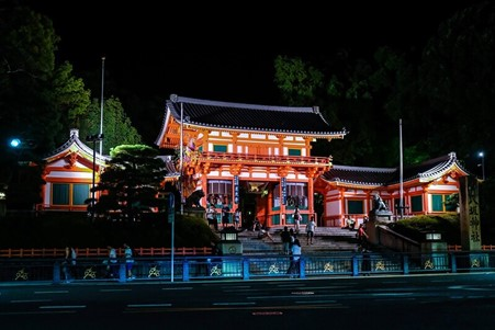 The yasaka shrine is lit up at night with people standing in front of it.