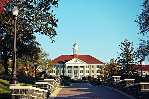 A large white building with a red roof is surrounded by trees in Harrisonburg
