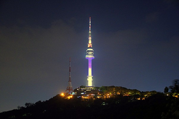 The N Seoul tower is lit up at night on top of a hill.