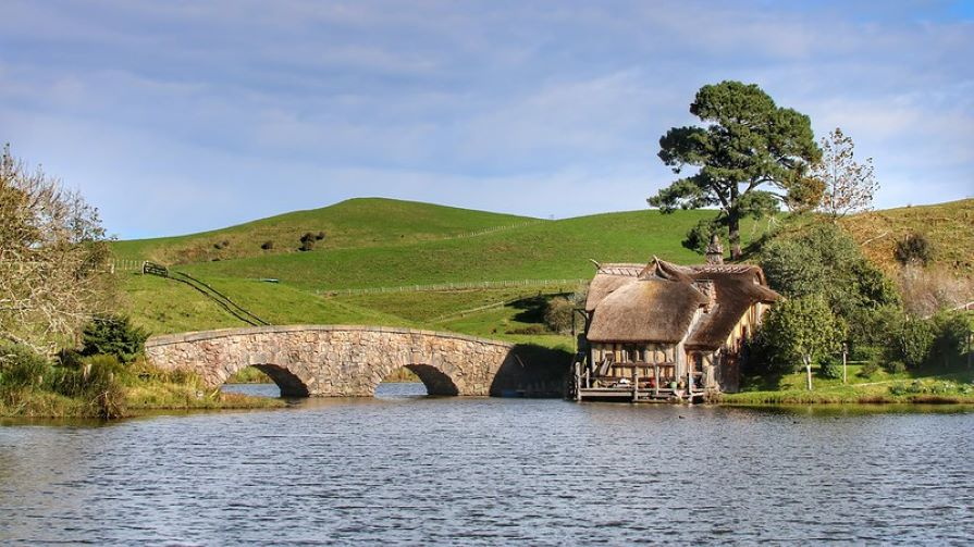 A stone bridge over a lake with a thatched hut in the middle from the shire