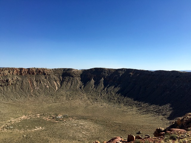 A large crater in the middle of a desert with a blue sky in the background at meteor crater natural landmark