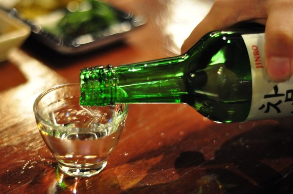 A person is pouring a glass of soju
