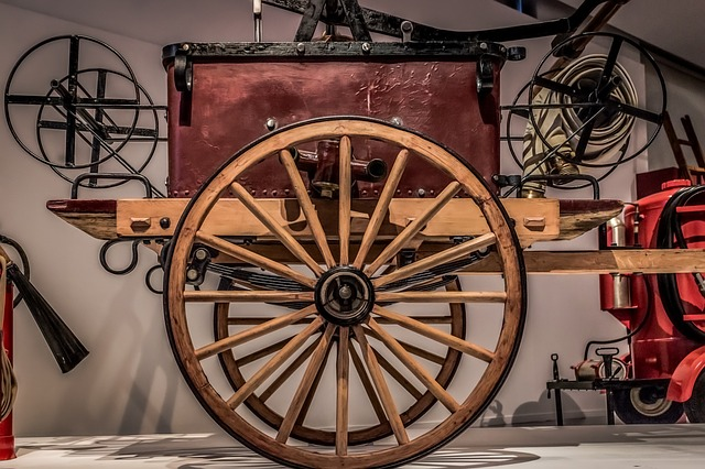 An old wooden wagon with a wooden wheel is sitting on a table in he hall of flame fire museum