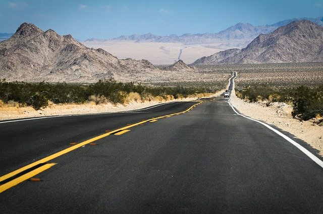 An empty road in the desert in the US with mountains in the background