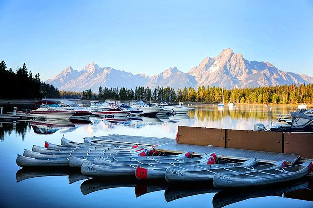 A dock in grand teton np filled with kayaks and boats on a lake with mountains in the background.