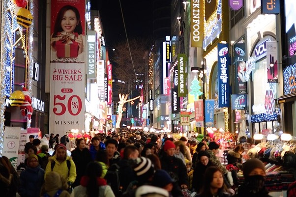 A crowd of people are walking down a busy Seoul street at night.