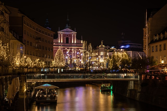 A bridge over a river in ljubljana at night with christmas lights on the buildings.