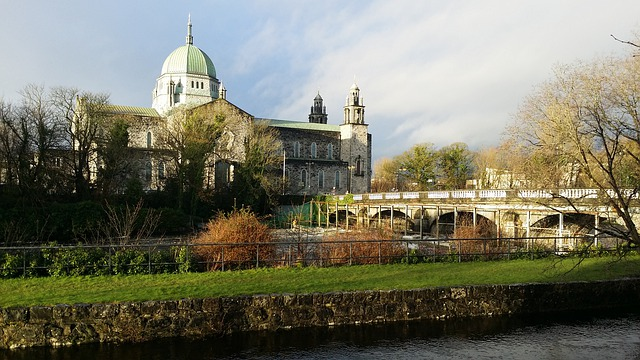 A bridge over a river in Galway with a large building in the background.