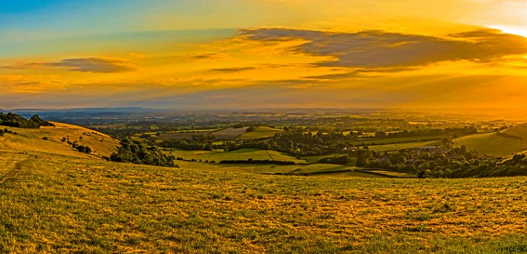 A panoramic view of a field in Cranborne Chase Area of Outstanding Natural Beauty,at sunset with a city in the distance.
