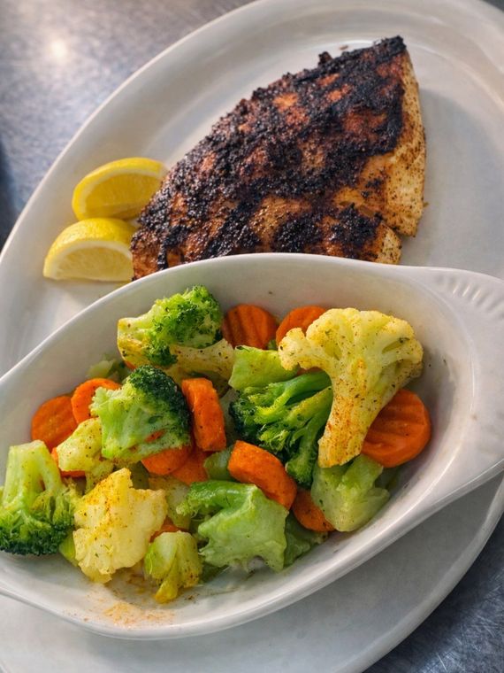 A seared fish fillet served with lemon wedges and a side of steamed broccoli and sliced carrots in a white dish.