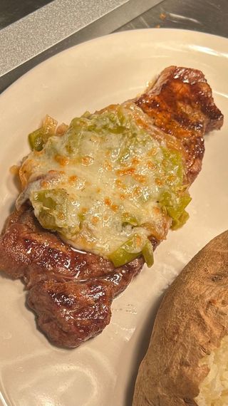 Grilled steak topped with melted cheese and chopped green chiles on a plate next to a baked potato.