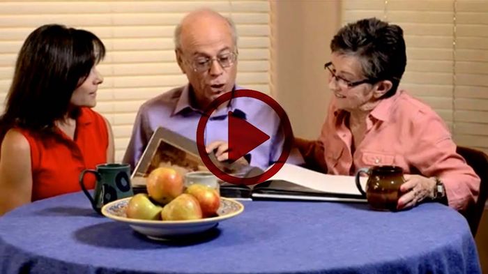 Three people sit at a round table with a bowl of apples, looking at a document and talking.