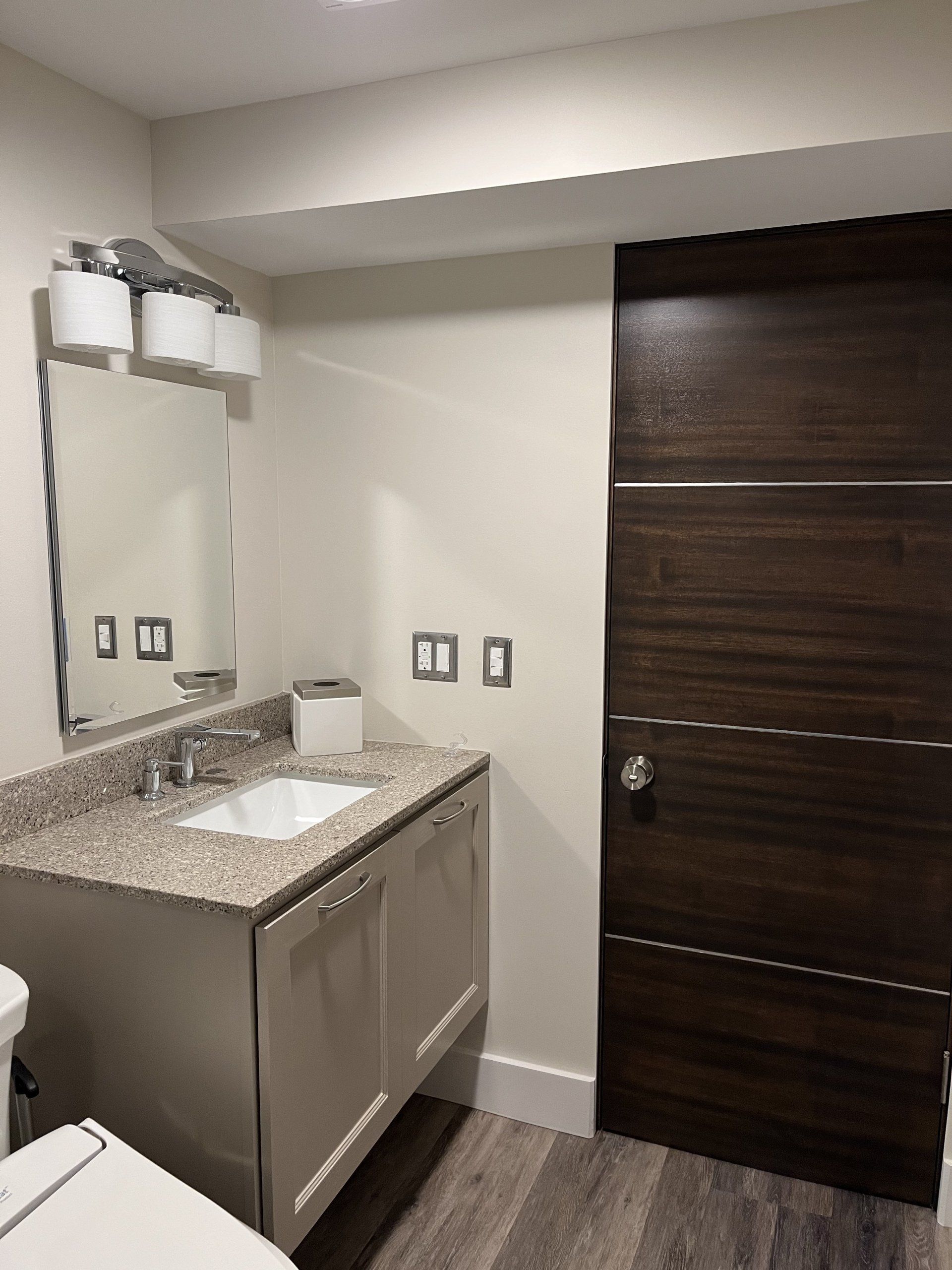 Small bathroom vanity with mirror, granite countertop, sink, and dark wood door.