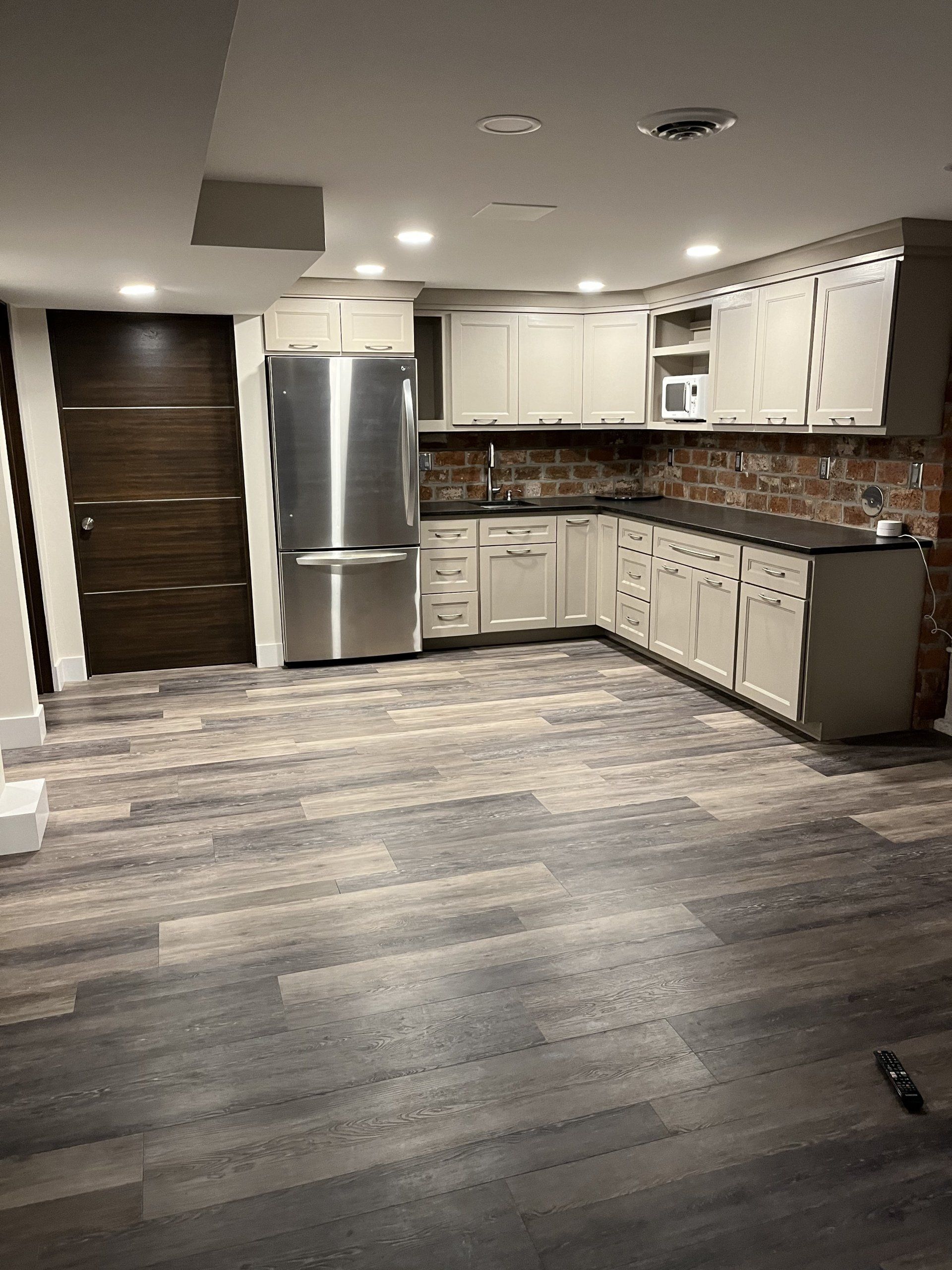 Empty modern kitchen with stainless steel fridge, white cabinets, and gray wood flooring