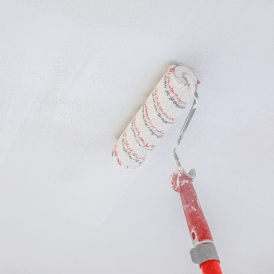 Paint roller with red handle and striped cover painting a white wall or ceiling