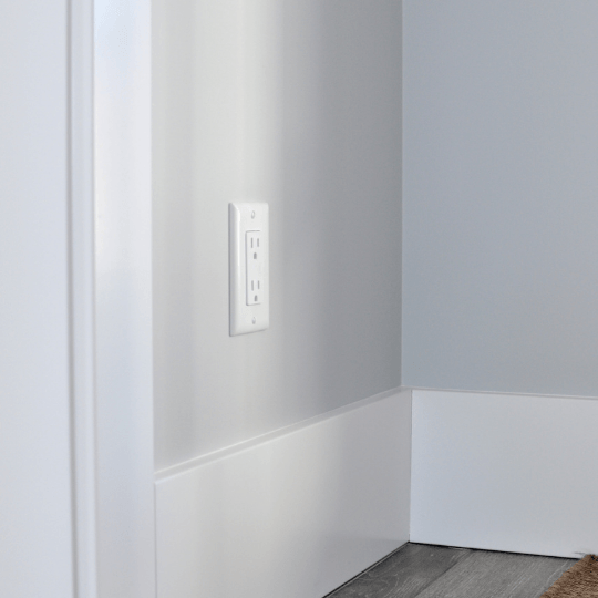 White wall with electrical outlet and baseboard in an empty room corner