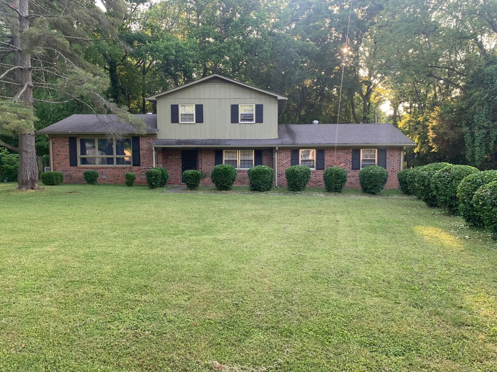 Brick house with a large green lawn and trees in the background