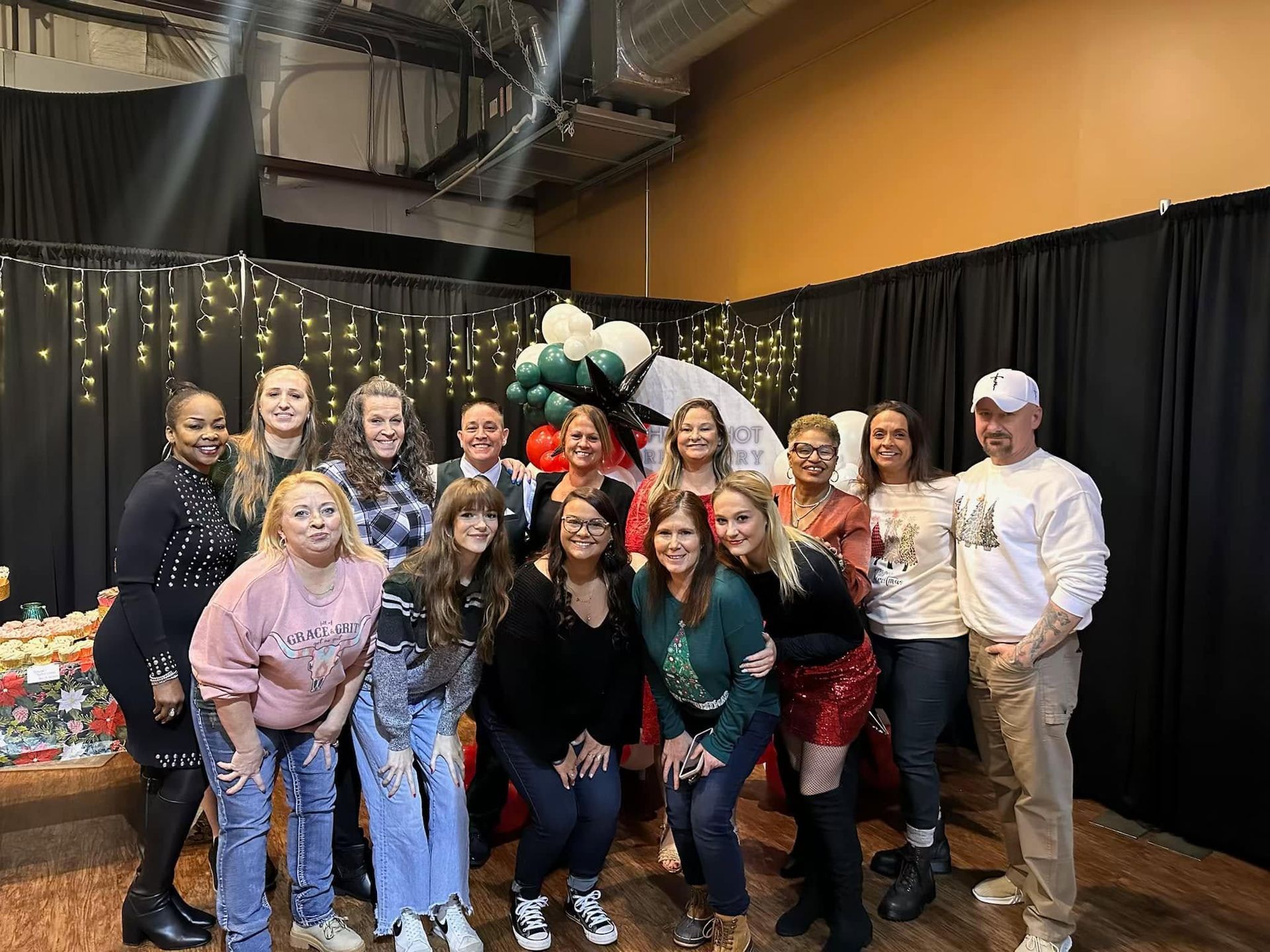 Group of smiling people posing indoors at a festive holiday event with balloons and a decorated backdrop