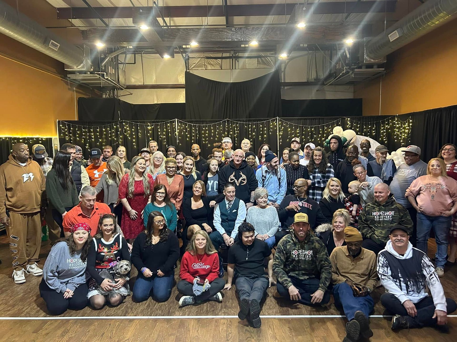 Large group photo of people posing in a decorated hall with string lights and black drapes