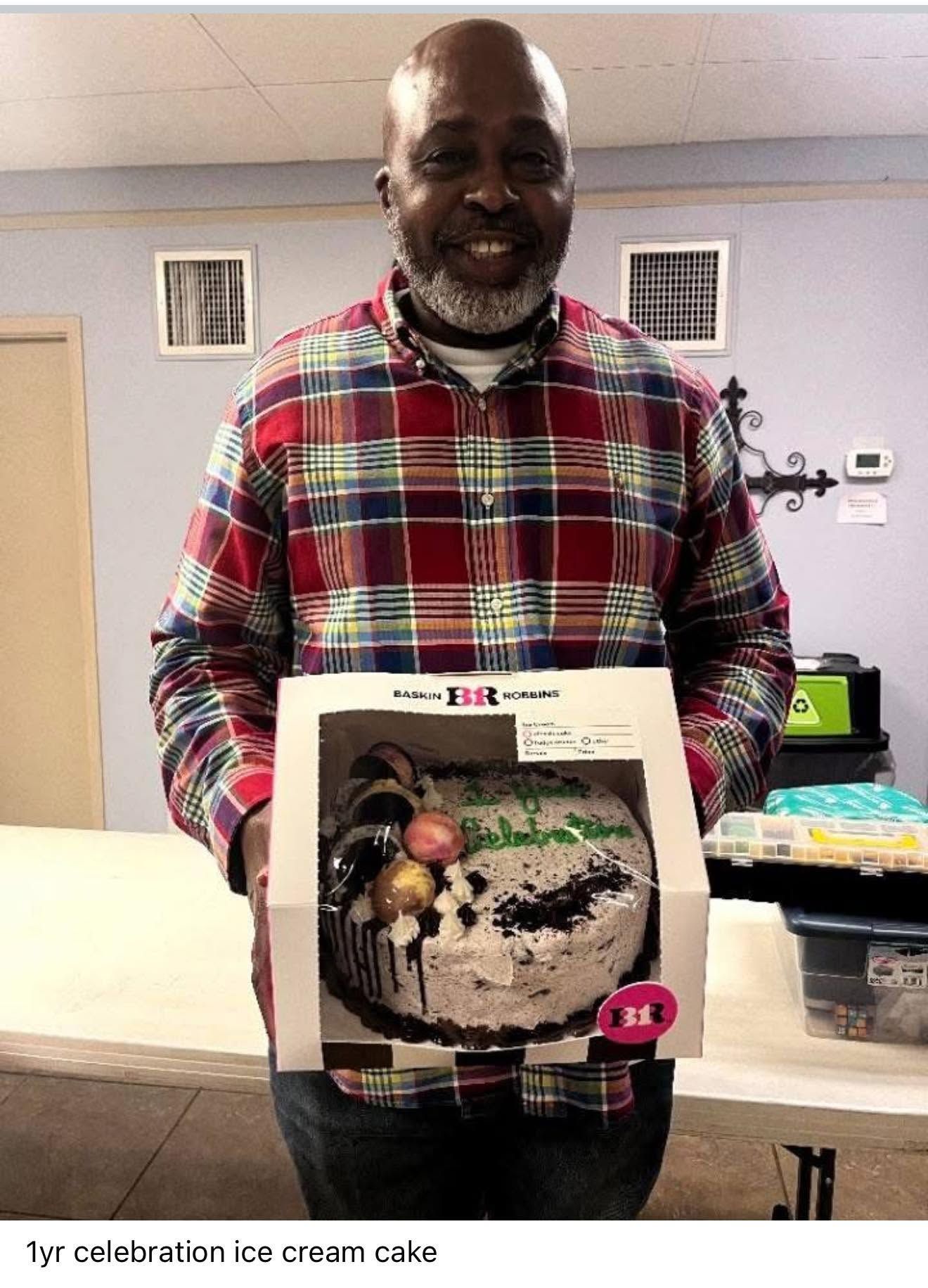 Man smiling and holding a boxed ice cream cake in an office break room
